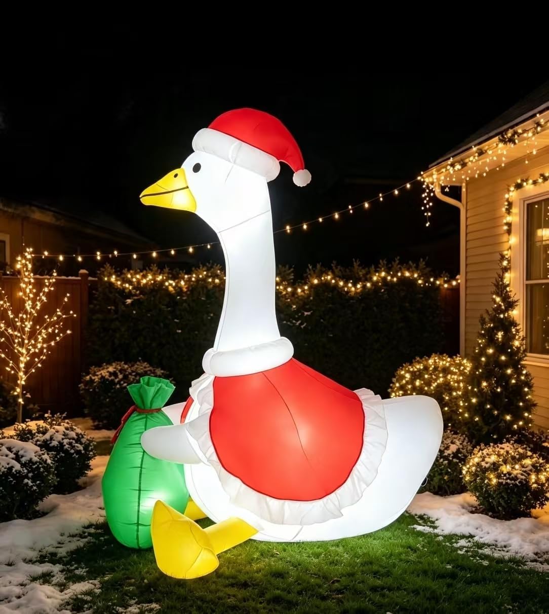 White goose inflatable in a Santa hat and red vest with a green gift sack on a lawn at night