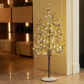 Slim lighted branch tree with warm lights and pine cones in a home entryway