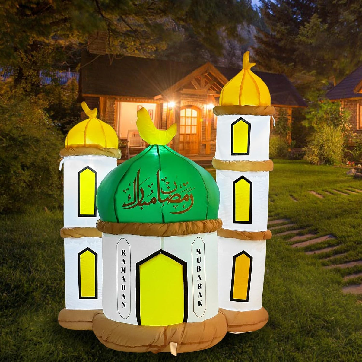 White mosque inflatable with a green dome, gold tower domes and a crescent on a lawn at dusk