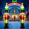 Two nutcracker soldier inflatables holding a Merry Christmas arch over a snowy front walk