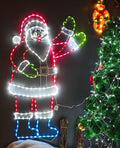 Neon-style LED outline of Santa waving in red, white, green and blue light beside a lit tree